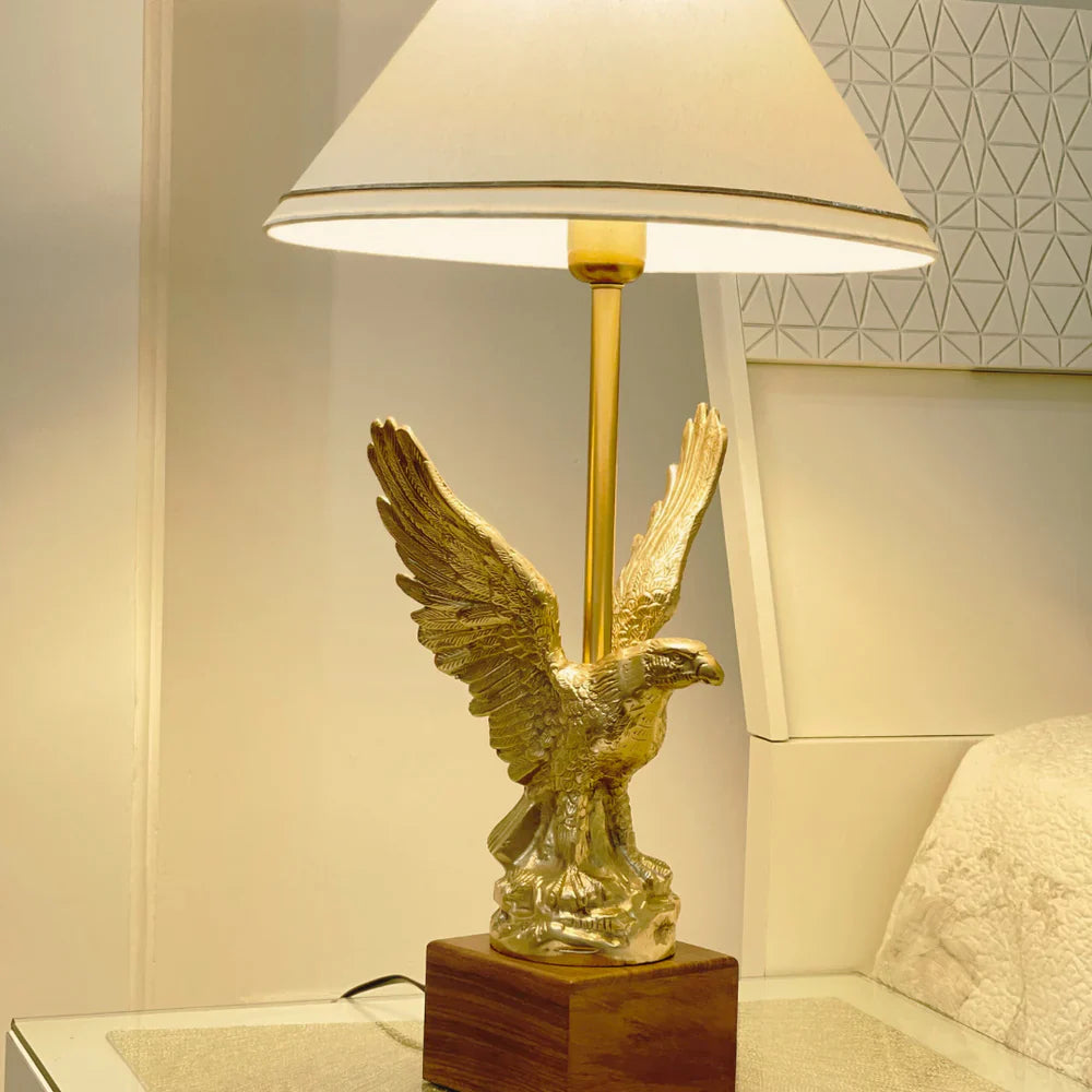 Gold eagle table lamp with white shade on wooden base.
