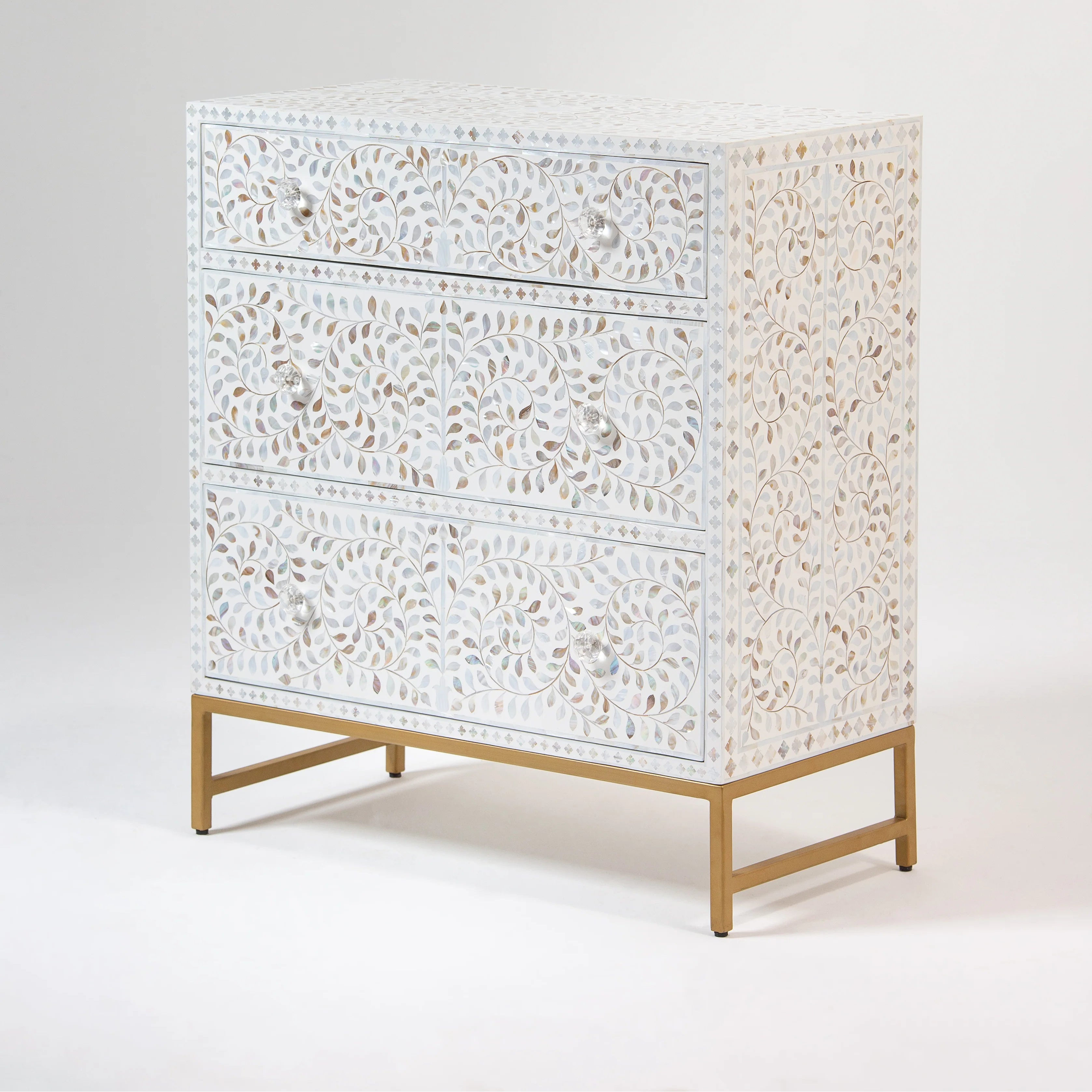 Side view of a bone inlay dresser with detailed swirl and leaf patterns, featuring crystal-clear knobs and supported by a sleek gold metal frame.