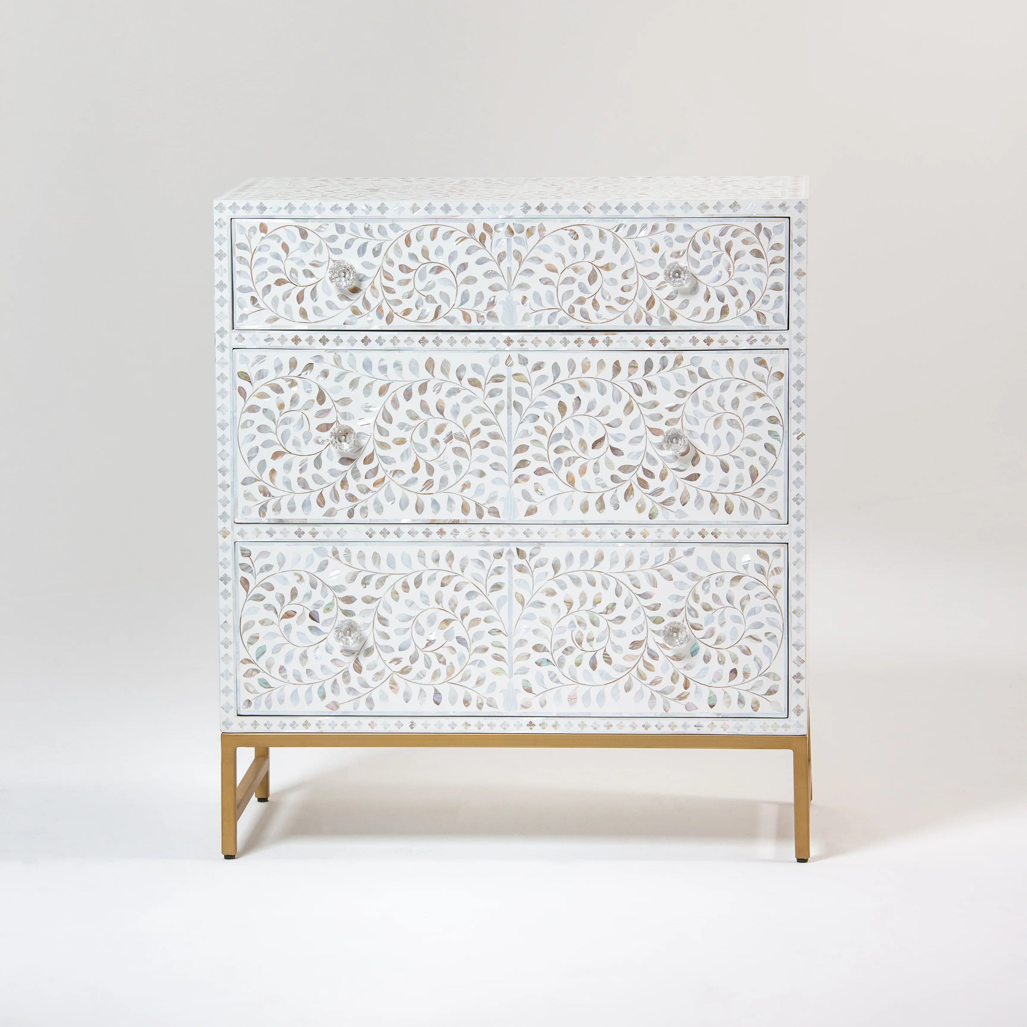 Decorative chest of drawers featuring intricate swirl and leaf carvings with crystal-clear knobs, set against a white background.