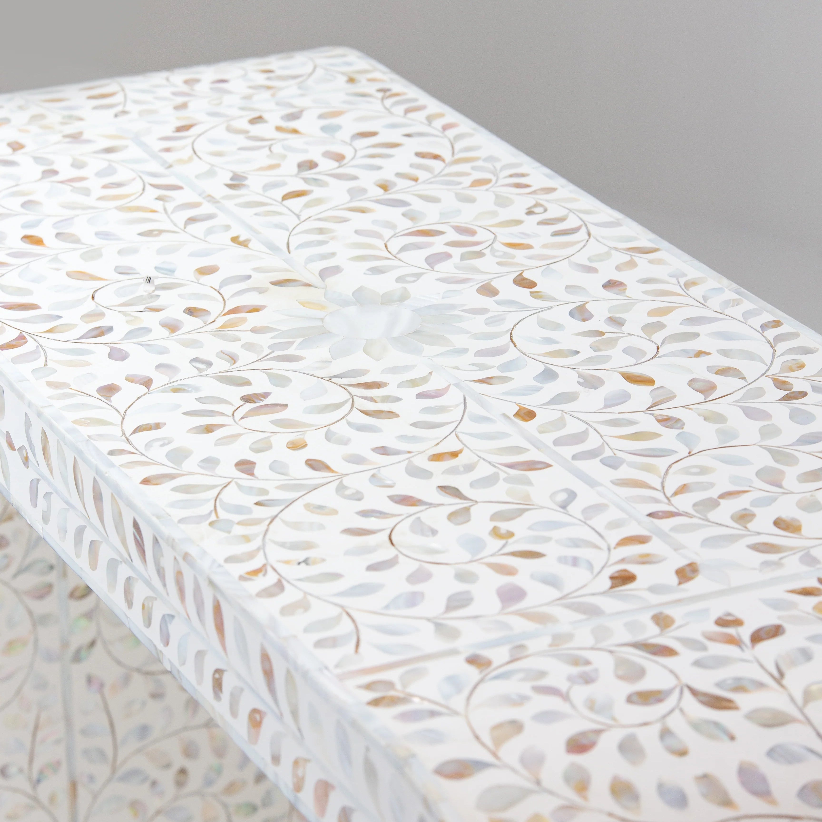 Close-up of a bone inlay table displaying detailed swirl and leaf patterns with a floral design in the center, focusing on the top surface.