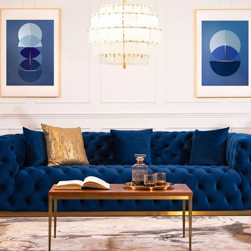 Luxury navy blue tufted sofa with gold accents, complemented by modern wall art and a stylish chandelier, showcasing elegant living room decor from Casagold Home Makeover.