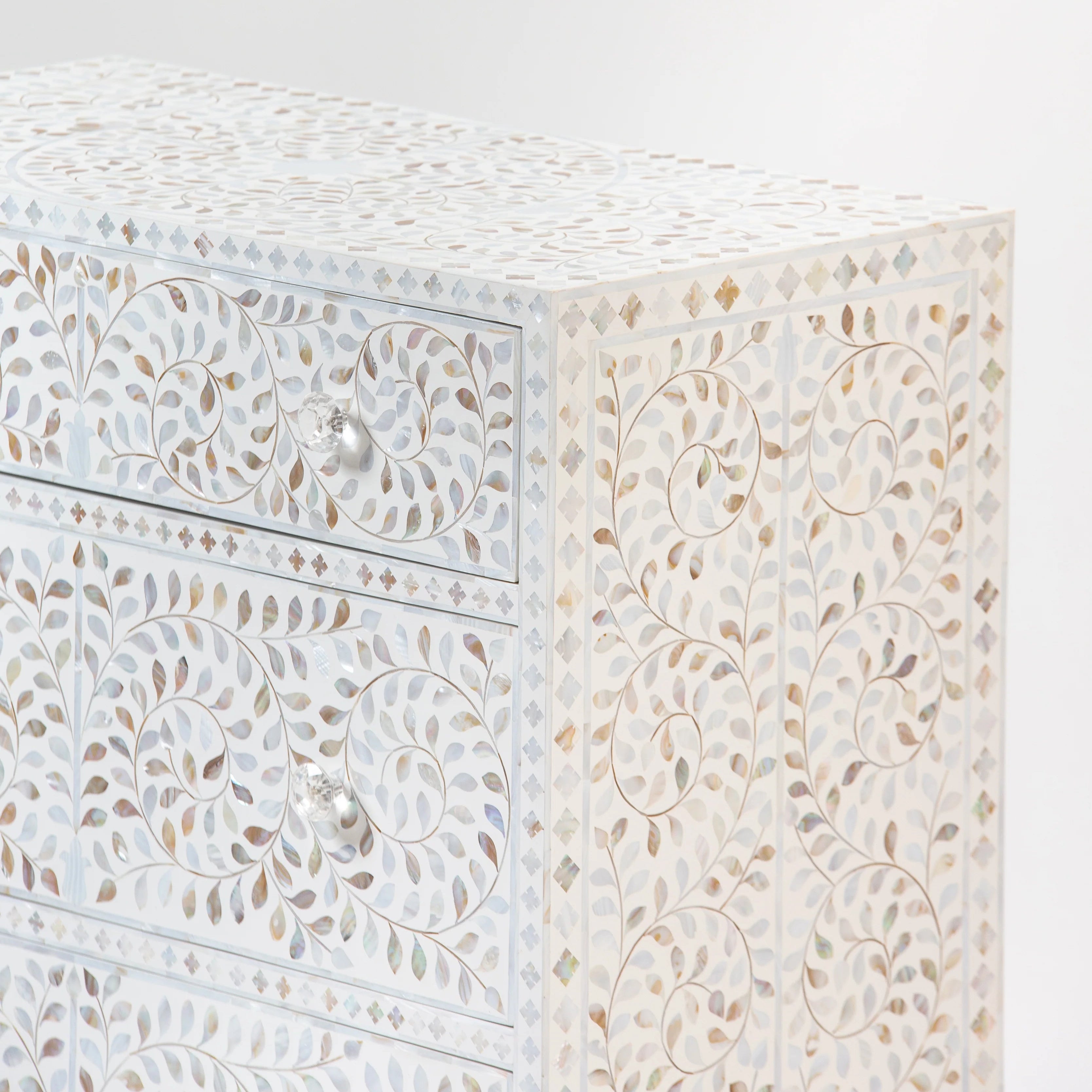Close-up of a bone inlay cabinet with intricate swirl and leaf patterns, featuring crystal-clear knobs and a detailed geometric design.
