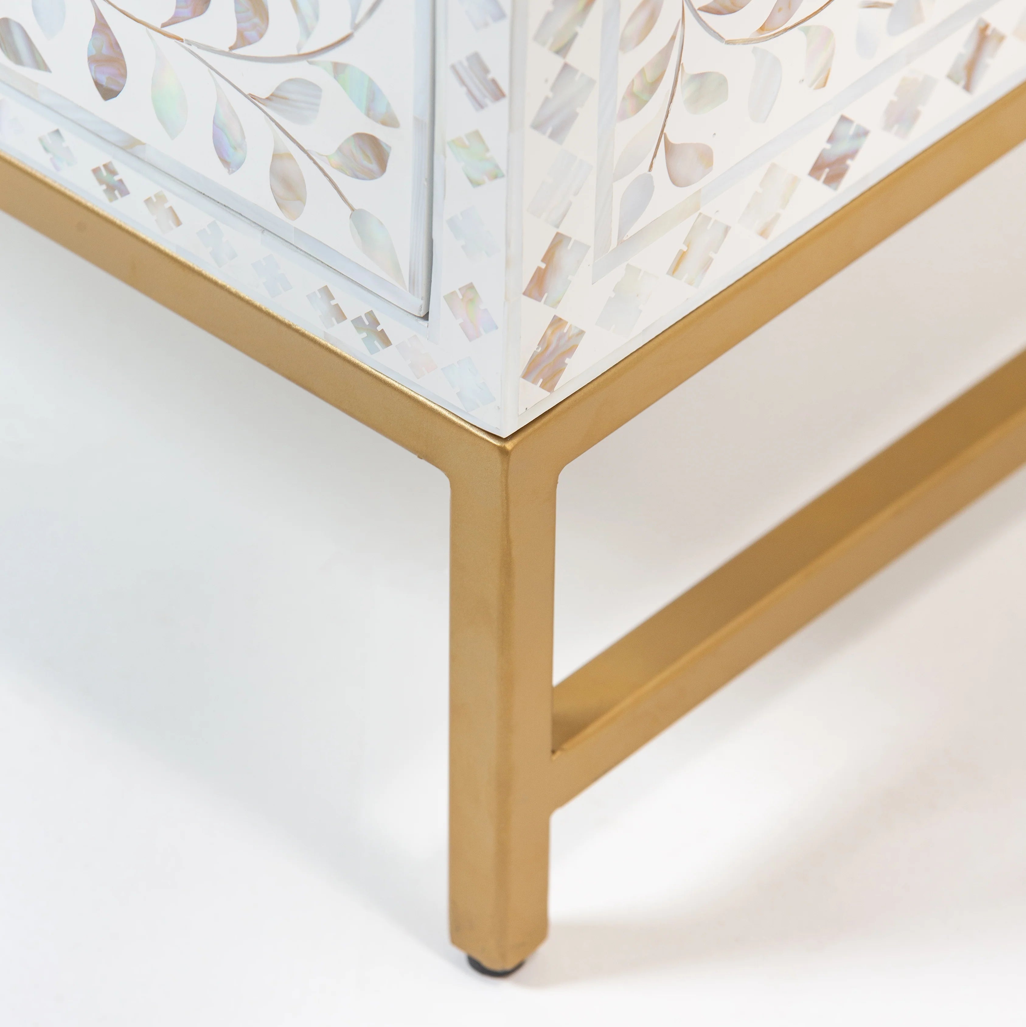 Close-up of a bone inlay cabinet with gold metal legs, showcasing intricate swirl patterns, against a plain white background.