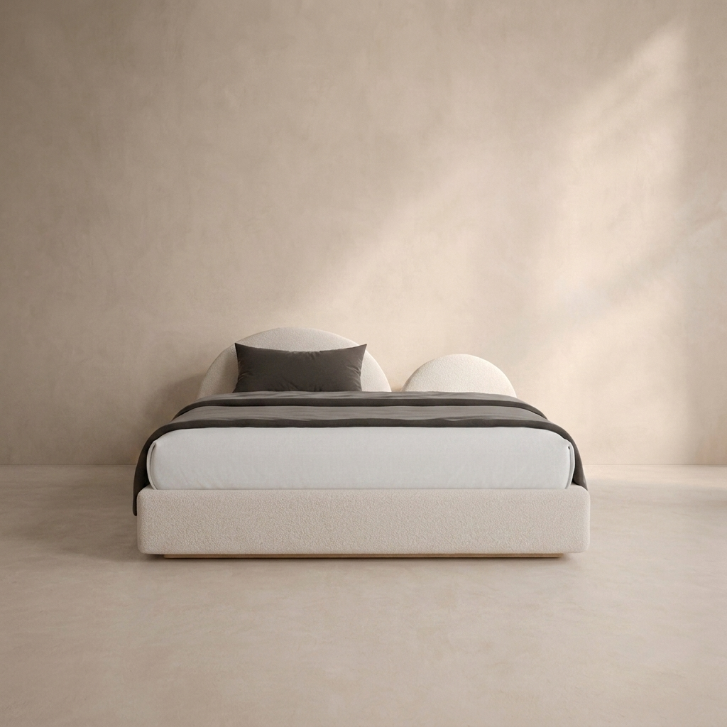 A modern low-profile platform bed with a textured cream upholstered frame, dressed in white bedding and a dark gray accent pillow, set against a minimalist beige plaster wall and floor.