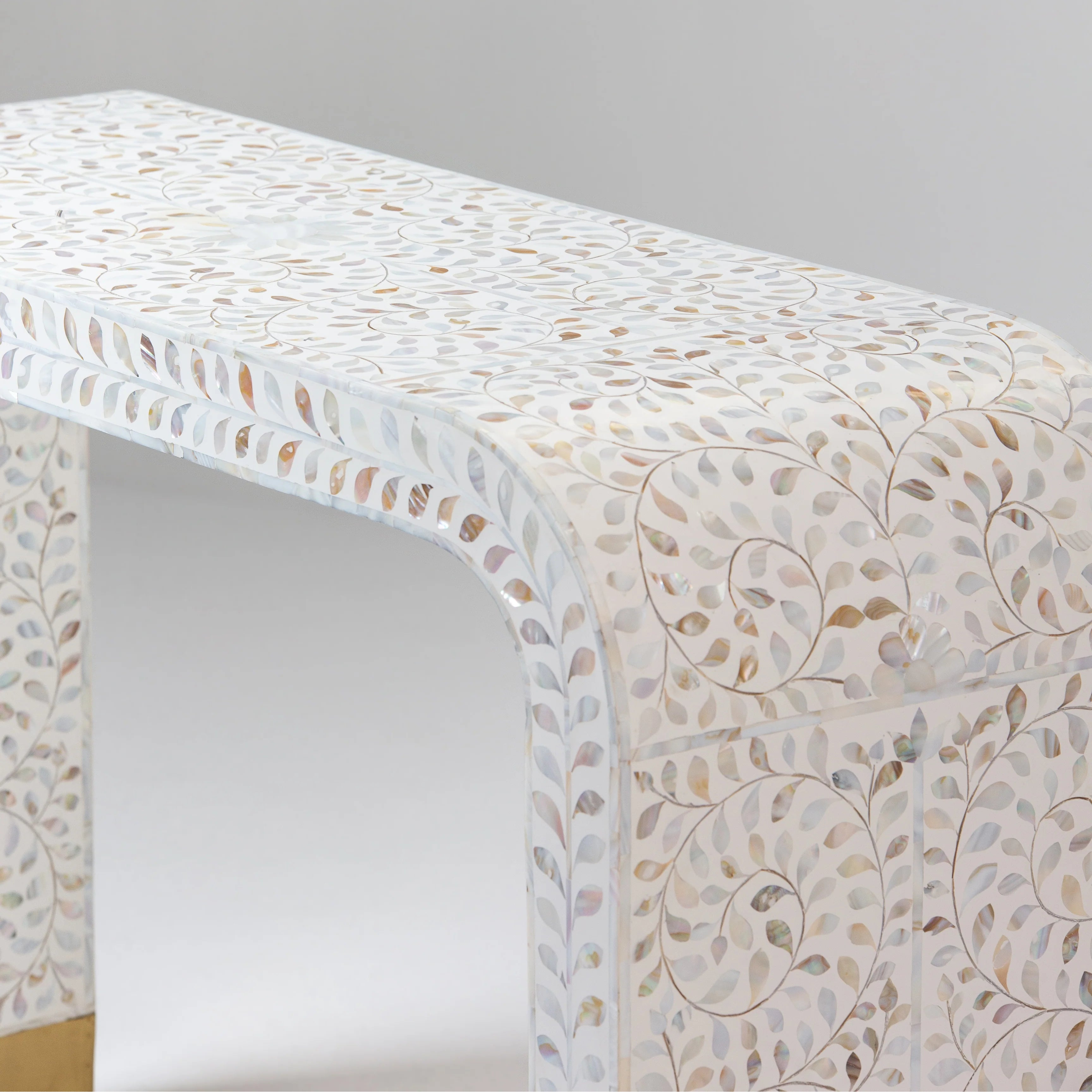 Close-up of a bone inlay table showcasing intricate swirl and leaf patterns, with attention to the top surface and rounded corners.