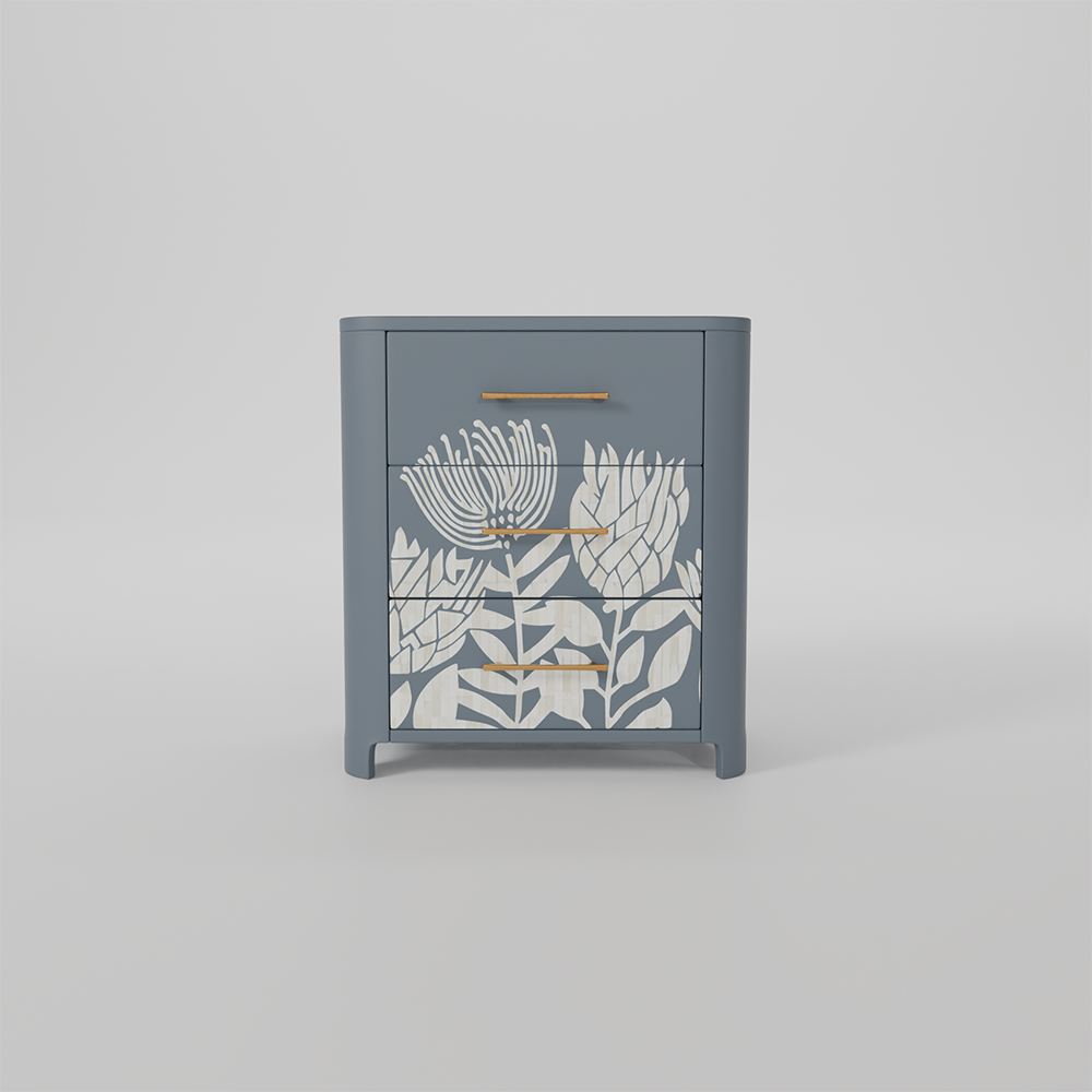 A small two-drawer nightstand in muted blue-gray with white floral inlay on the drawer fronts and slim gold-tone metal handles, shown against a light gray studio background.