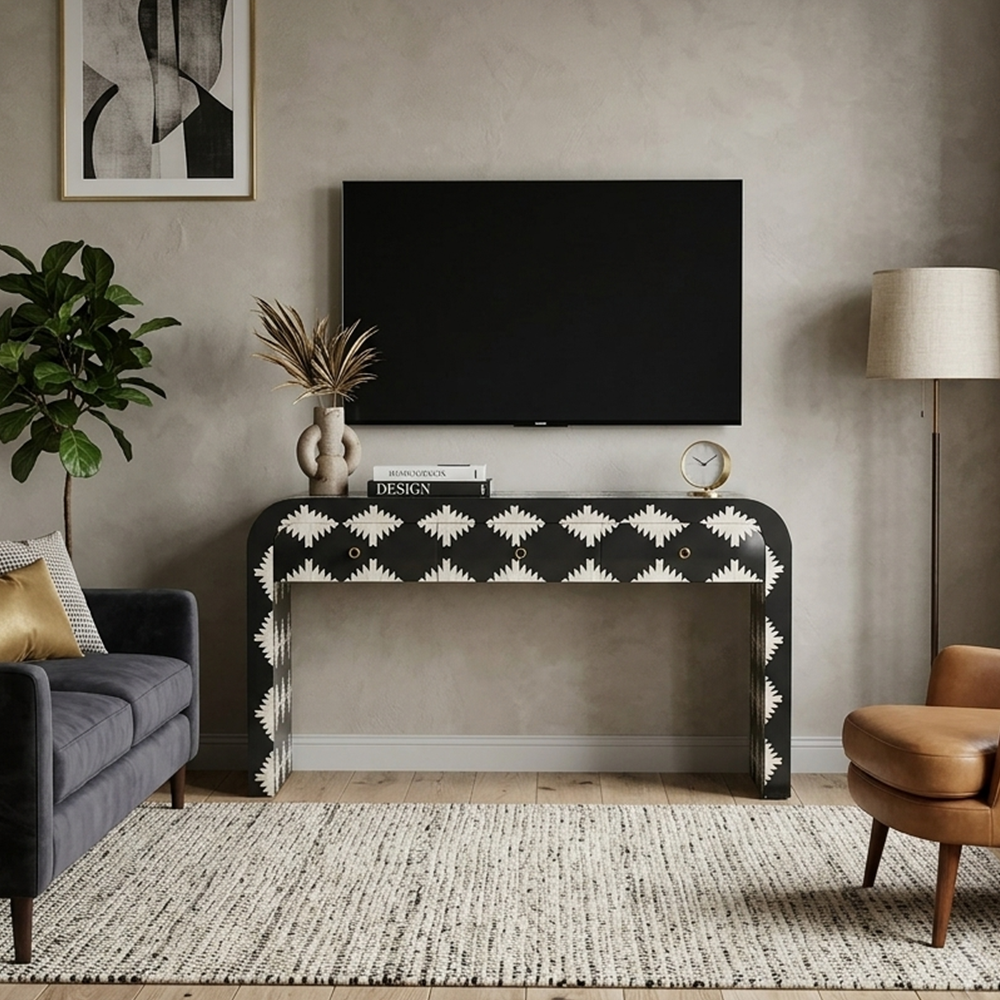 A black console table with a white geometric pattern, styled in a modern living room setting with a TV on top, a sofa, and a lamp.